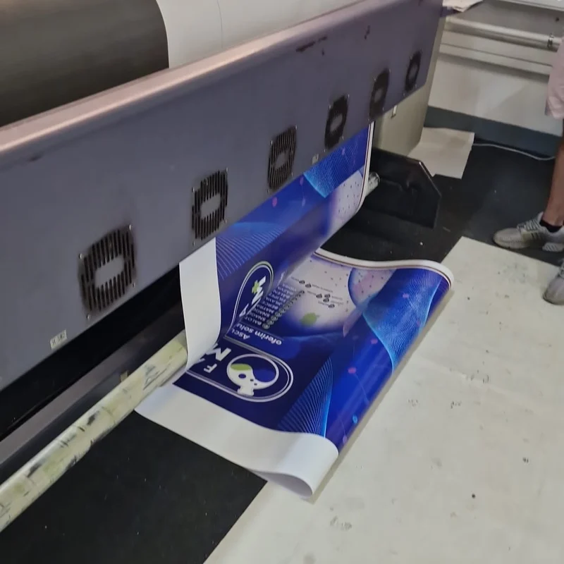 Banner publicitar full color pentru un client din reteaua de farmacii, in curs de printare pe o imprimanta large-format in atelierul Mora Group — print eco-solvent pe material PVC, vedere reala din productie