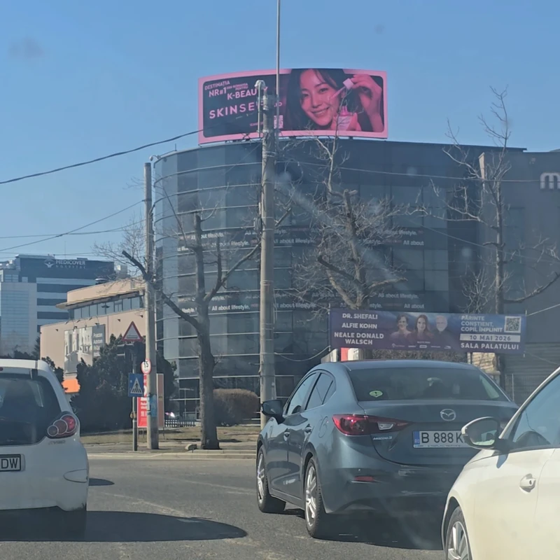 Vedere ansamblu panou digital LED pe acoperis la intersectia Sos. Fabrica de Glucoza cu Petricani, Bucuresti — campanie cosmetice ingrijire ten client cosmetice ten cu cladire moderna in fundal si trafic auto in nodul Floreasca-Pipera