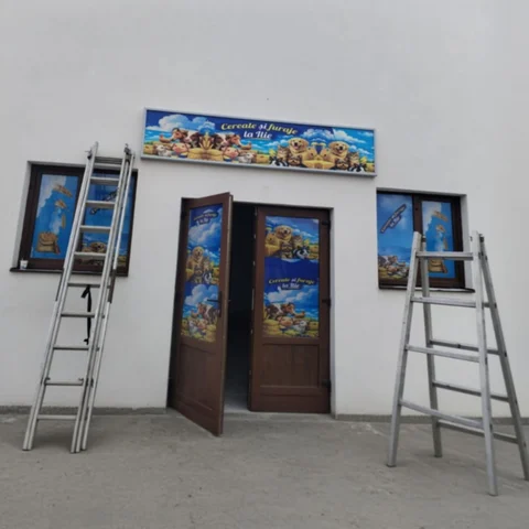 Vedere ansamblu montaj finalizat magazin Cereale si furaje la Ilie cu caseta luminoasa LED deasupra usii si window graphics pe ferestre si usi — flux complet branding identity realizat de Mora Group, 2 scari metalice profesionale pe fatada exterioara dupa instalare