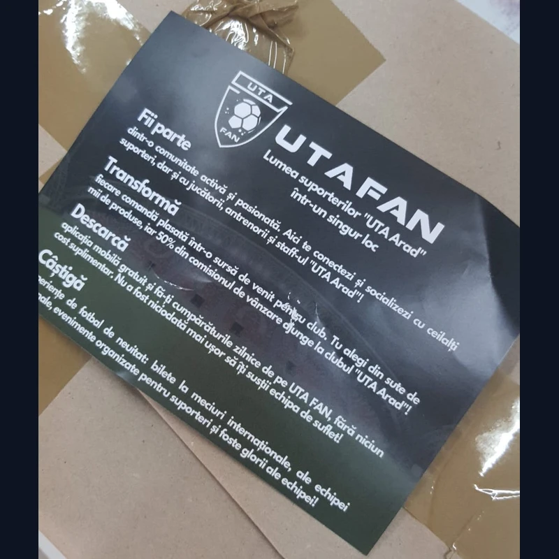 Detaliu flyer client fan club fotbal local verso cu text descriere aplicatie mobila si sigla club, asezat pe pachet ambalat in atelierul Mora Group inainte de livrare