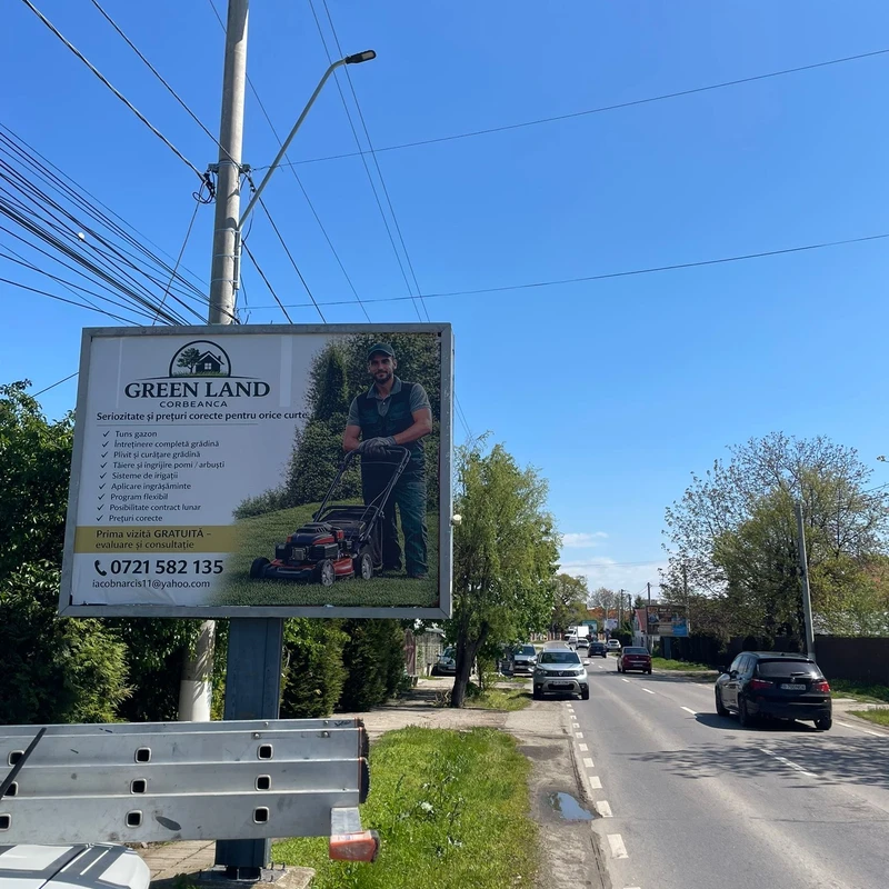 Panou outdoor 5×4 m produs si montat de Mora Group pentru client amenajari gradini din Corbeanca — banner PVC frontlit cu fotografie servicii (om cu masina de tuns gazon) pe structura metalica pe stalp langa drumul judetean DJ Corbeanca, cer senin de zi insorita
