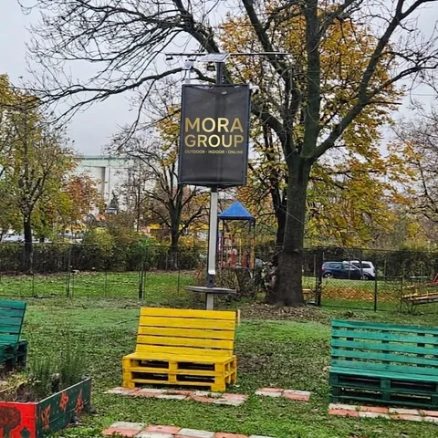 Stalp solar Mora Group cu banner publicitar instalat in curtea unei scoli gimnaziale, vedere generala cu mobilier urban si banci colorate