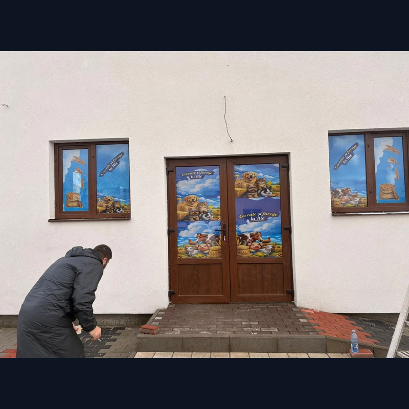 Window graphics aplicate close-up pe usile magazinului Cereale si furaje la Ilie — autocolante PVC perforate one-way vision cu grafica brand, animale de ferma si saci de cereale pe ferestre si usi
